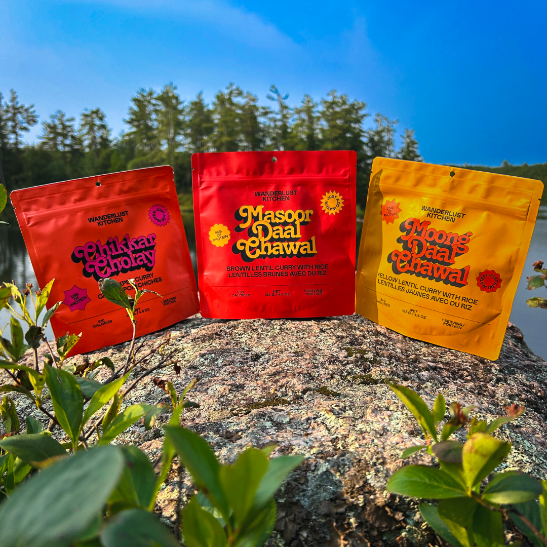 Three ready to eat camping meals in front of a lake